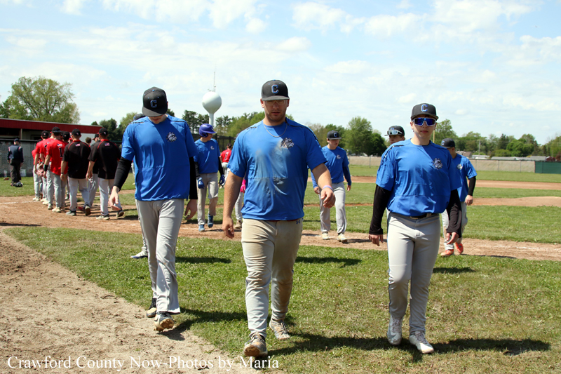 Group of baseball players in blue shirts walk together on a baseball field, central player leading toward the camera.