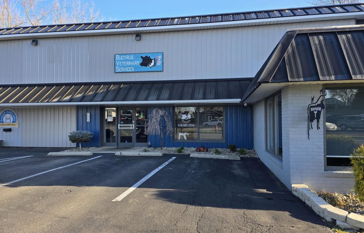 Exterior view of Bucyrus Veterinary Services building with blue sign, glass doors, and a parking lot nearby