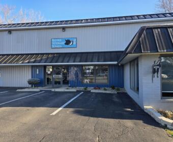 Exterior view of Bucyrus Veterinary Services building with blue sign, glass doors, and a parking lot nearby