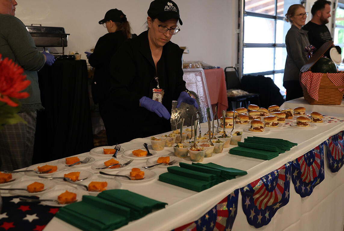 Food buffet at a patriotic event with sandwiches, bowls of tapas, and orange-tinted desserts on a long table covered in a stars-and-stripes tablecloth.