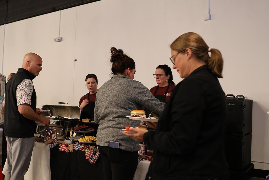 People line up at a buffet table indoors, serving themselves food at a casual event hall.