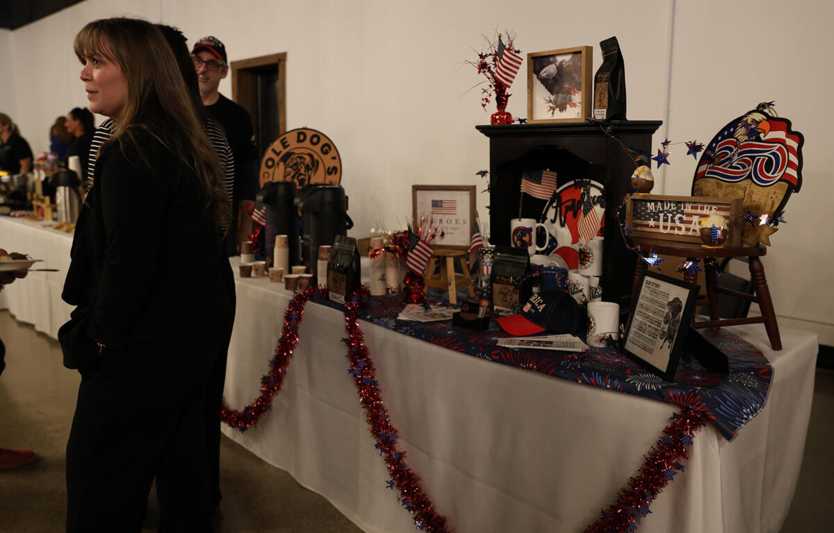 People browse a long table of patriotic gifts and decorations, with red, white, and blue garlands draped along the edge.