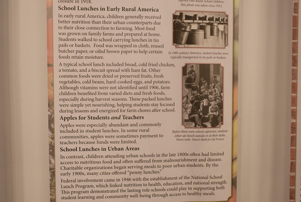 Tall banner poster about the Harvey One-Room School, titled 'Student Lunchtime in Early America,' with historical text and several black-and-white photos along the right side and a photo of a brick school at the bottom.
