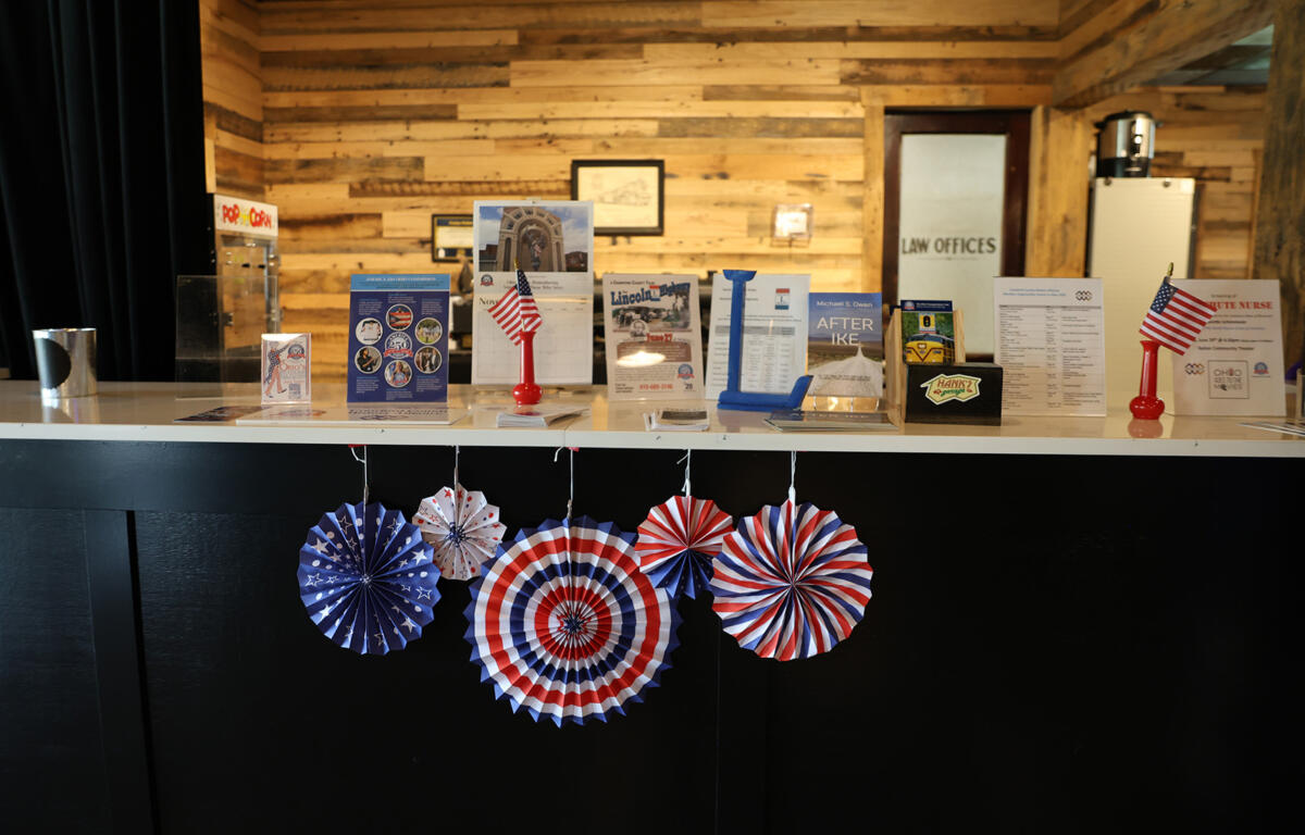 Reception counter with patriotic red, white, and blue paper decorations and brochures in a wood-paneled room on display shelves and stands nearby.