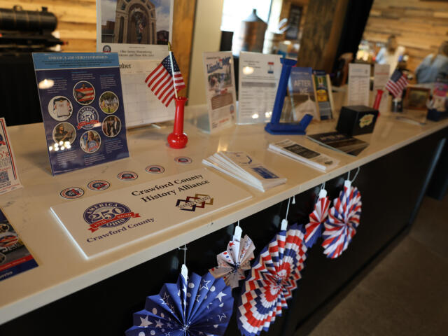 Patriotic display at a information desk with brochures, brochures stands, an American flag, and red‑white‑blue pinwheels on a white counter.