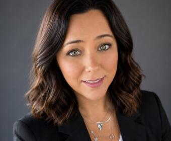 Portrait of a smiling woman with shoulder-length brown hair in a black blazer, looking at the camera.