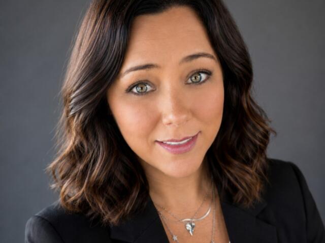 Portrait of a smiling woman with shoulder-length brown hair in a black blazer, looking at the camera.