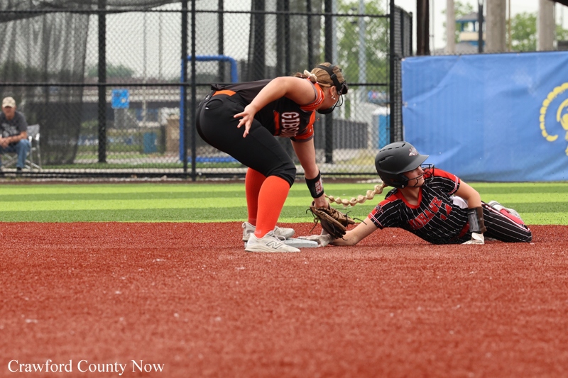 Two female softball players contest a play at a base: one slides in with a helmet and striped uniform, the other bends to tag on the red dirt.