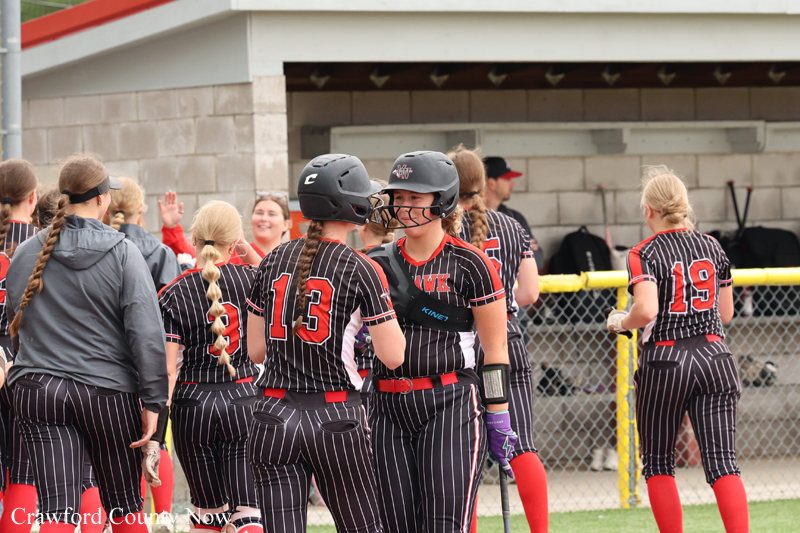 Girls in black pinstripe softball uniforms high-fiving near the dugout after a game.