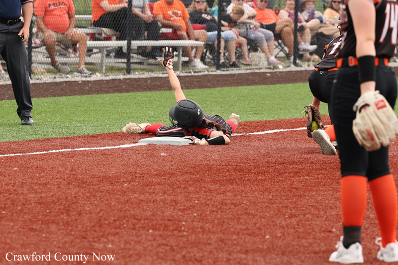 Softball player slides into home plate with arm raised as crowd watches from behind the fence.