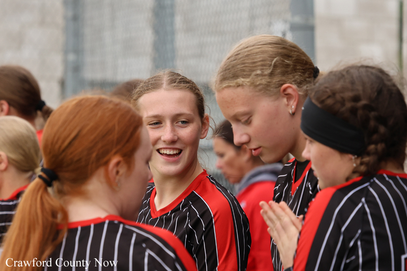 Group of female athletes in black-and-red striped uniforms chat and smile together before a game.