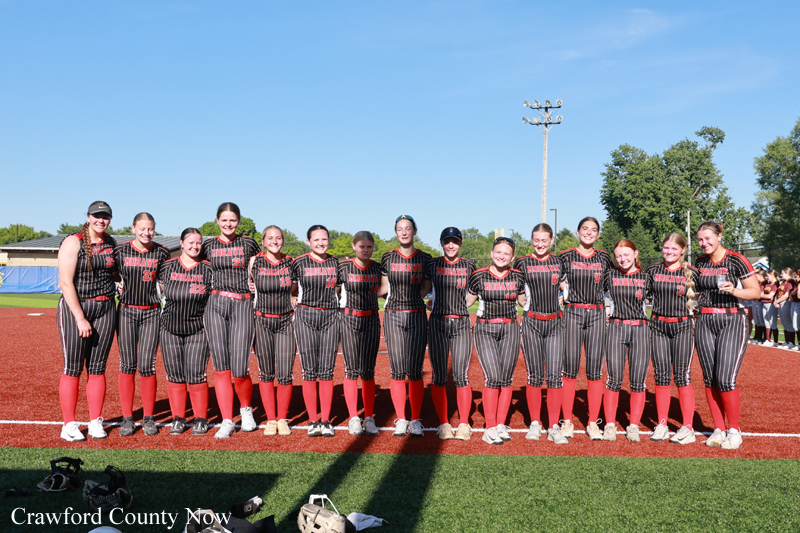 Softball team lined up for a photo on the field in striped black-and-red uniforms and red socks.