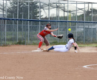 Baserunner slides into a base as a fielder stretches to tag, dust kicking up on the dirt infield.