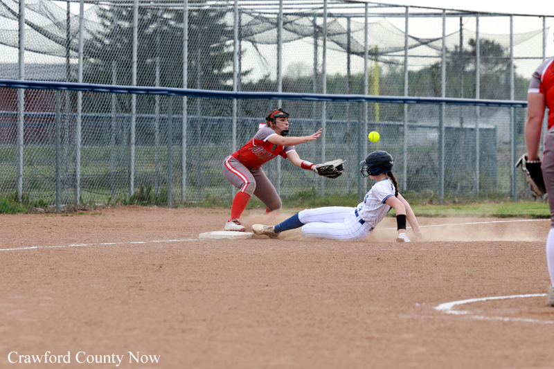 Baserunner slides into a base as a fielder stretches to tag, dust kicking up on the dirt infield.