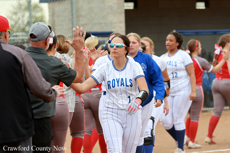 Softball players from the Royals team high-five teammates at the field during a game.
