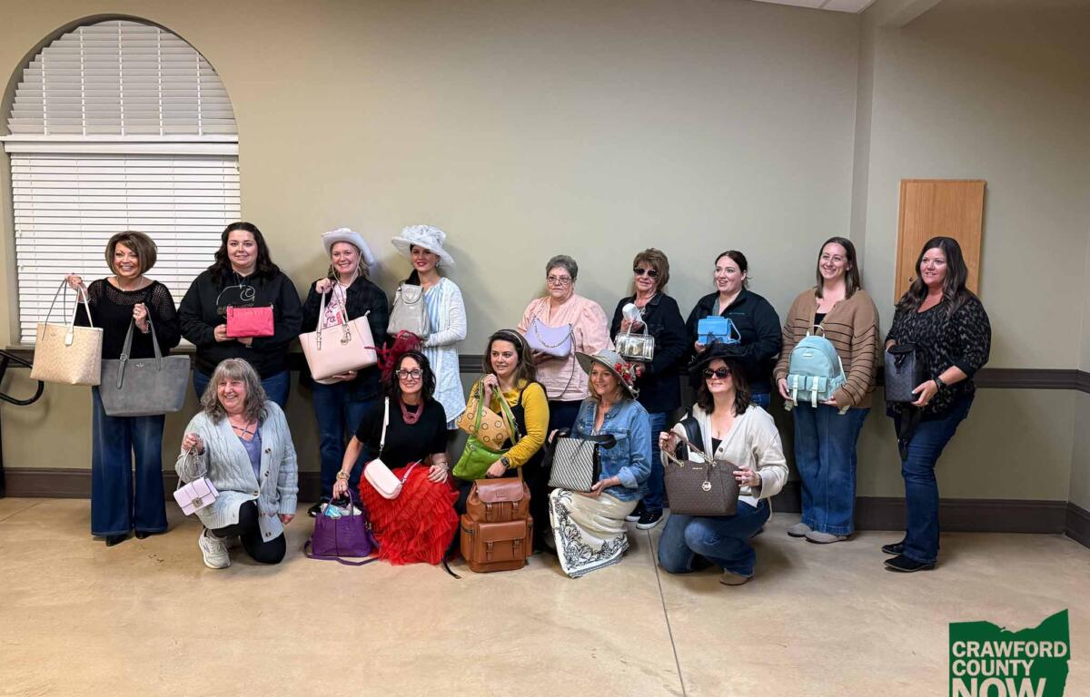 Group of women posing indoors with various handbags, some wearing hats, Crawford County Now logo visible in the bottom right corner