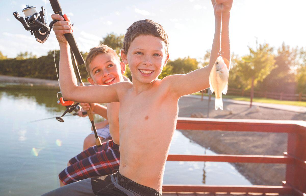 Two smiling boys on a dock with fishing rods, one proudly holding up a small fish.