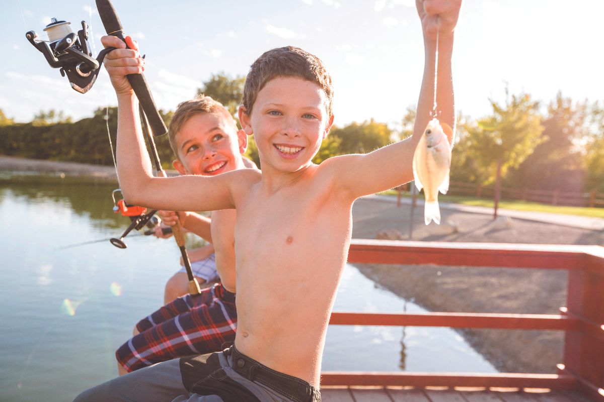 Two smiling boys on a dock with fishing rods, one proudly holding up a small fish.