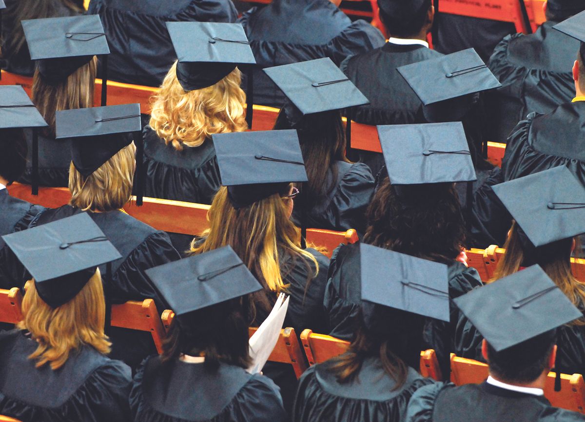 Rows of graduates in blue gowns and mortarboard caps seated in an auditorium with orange seats visible.