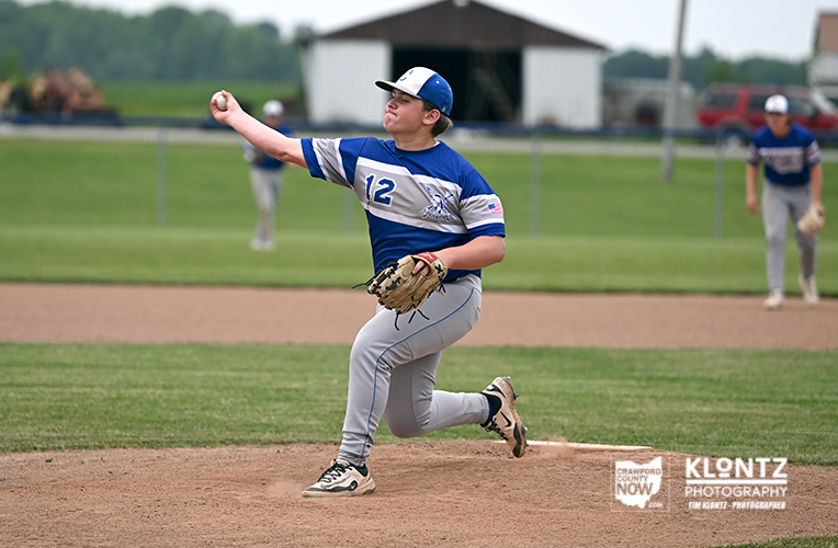Baseball pitcher in blue and white uniform delivering a pitch on the mound with the right arm extended and left foot forward on a dirt mound.