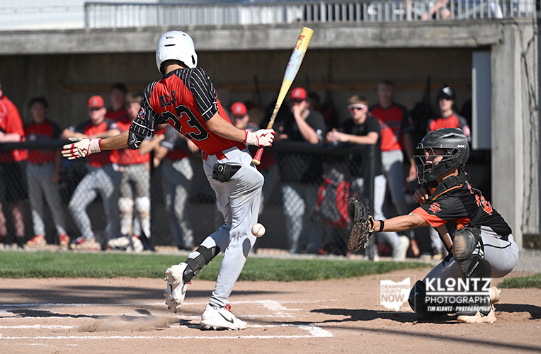 Baseball batter in a white helmet swings at a pitch while the catcher in black crouches behind home plate.