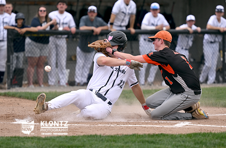 Baseball play at home plate: sliding runner in white and catcher in black and orange reach to tag as dust rises.