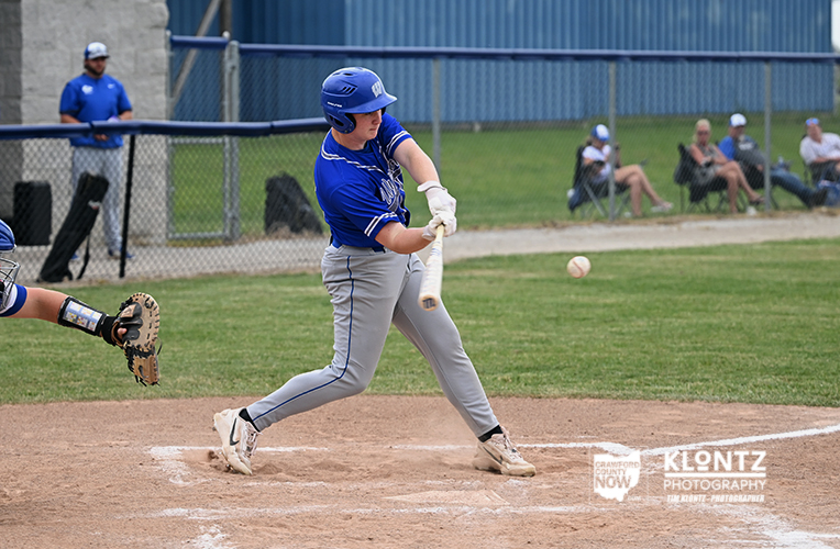 Baseball batter in blue uniform swings at a pitch near home plate as the catcher watches from behind the plate.