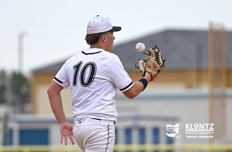 Baseball player in white uniform with number 10 preparing to catch a ball with his glove on a sunny field.