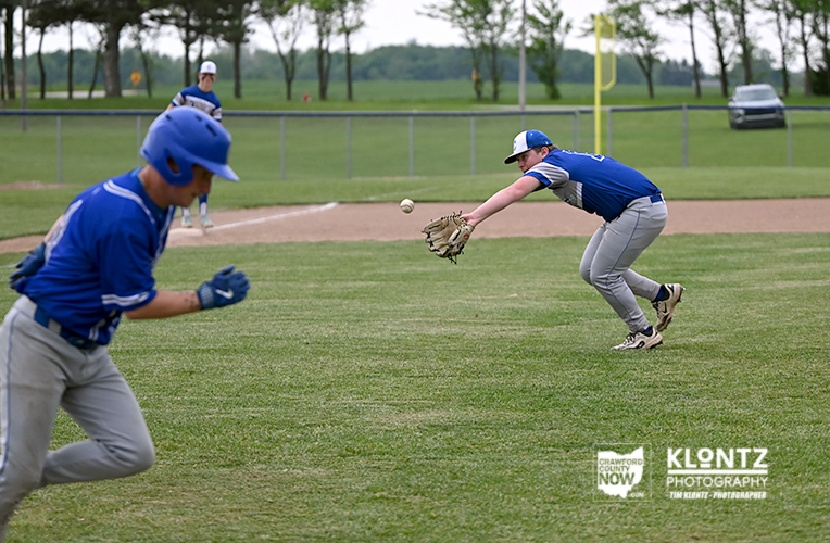 Baseball game: a fielder dives to catch a low ball with glove outstretched while another player runs in foreground on a grassy infield.