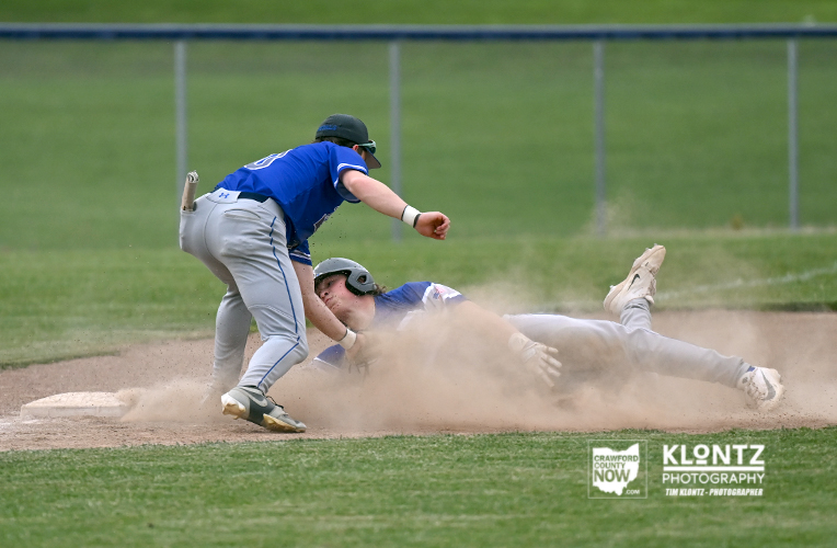 Baseball: fielder in blue lunges while a baserunner slides into a base, dust clouds the dirt.