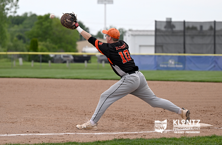 Baseball pitcher in a black-orange uniform delivers a pitch on the dirt mound, glove raised as the ball leaves the hand.