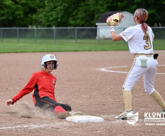 Softball scene: a baserunner slides into a base as a fielder in white prepares to tag.