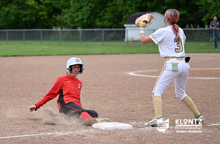 Softball scene: a baserunner slides into a base as a fielder in white prepares to tag.