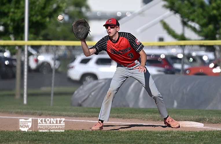 Baseball infielder in red and black uniform with glove raised, fielding near first base as a ball arrives.