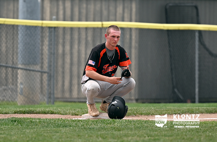 Baseball player in a black and orange uniform kneels on the pitcher's mound with his helmet on the ground nearby.