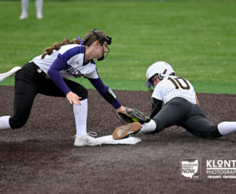 Softball player slides into first base as fielder reaches to tag her at the bag on a dirt infield