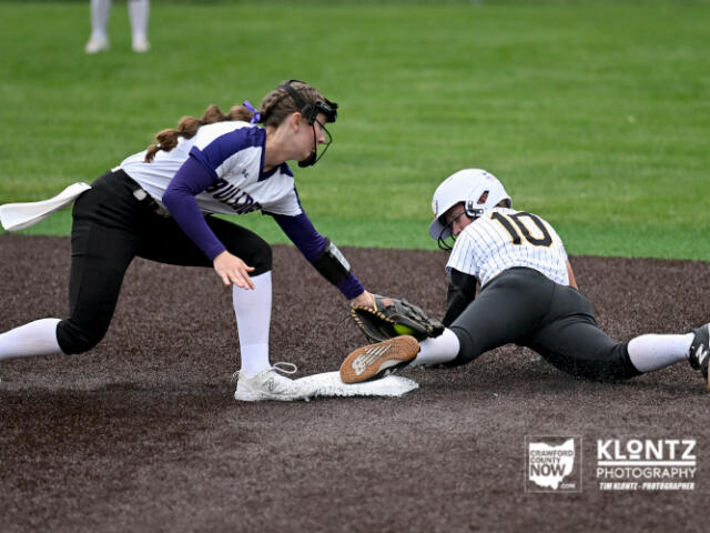 Softball player slides into first base as fielder reaches to tag her at the bag on a dirt infield