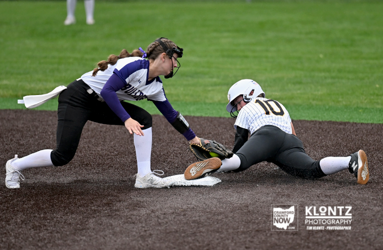 Softball player slides into first base as fielder reaches to tag her at the bag on a dirt infield