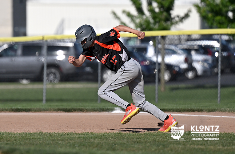 Baseball player sprinting along the baselines in a black-and-orange uniform with a helmet and red cleats.