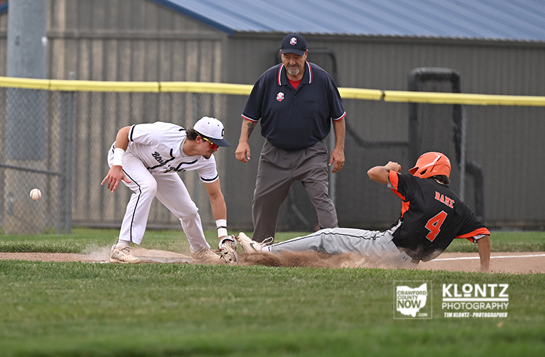 Baseball play at second base: fielder in white reaches for the bag as a runner in black slides, ball in the air and dust around the base, with an umpire watching.