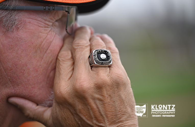 Close-up of a man's hand near his face, wearing a large silver ring with a black square centerpiece and glasses nearby.