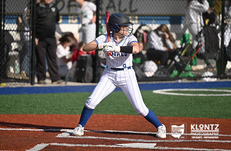 Young baseball player in a white pinstripe uniform swings a bat at home plate during a game.