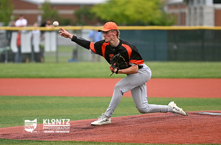Baseball pitcher in orange cap and black-orange jersey delivering a pitch on the mound with the ball midflight.