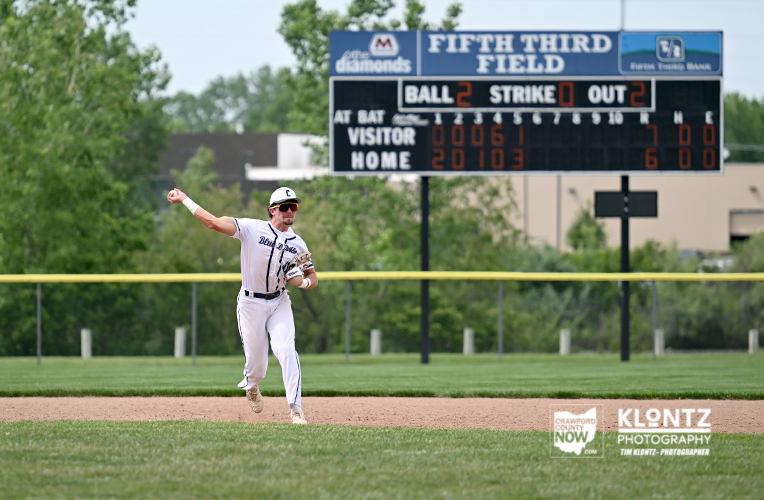 Baseball player in a white uniform throws from the infield with a scoreboard in the background.