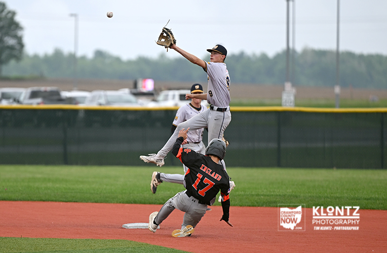 A baseball fielder in white uniform leaps to catch a high throw while a baserunner in black #17 slides into base on the dirt infield.