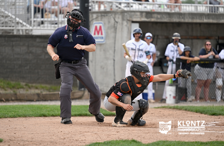Baseball catcher slides into home plate as the umpire closes in and teammates watch in the background.