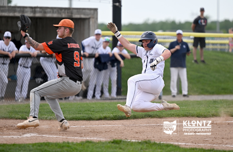 Baseball runner slides into a base as a fielder reaches to tag him near a dirt infield with spectators in the background.