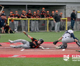 Baseball player slides headfirst into home plate as catcher reaches to tag him; umpire watches nearby.