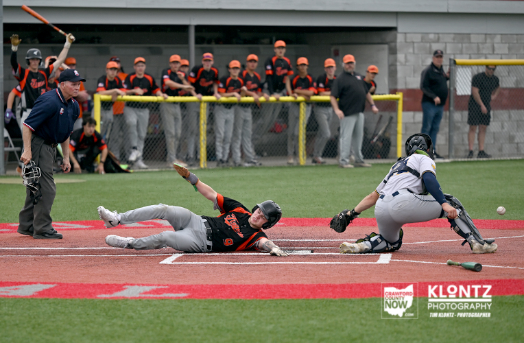 Baseball player slides headfirst into home plate as catcher reaches to tag him; umpire watches nearby.