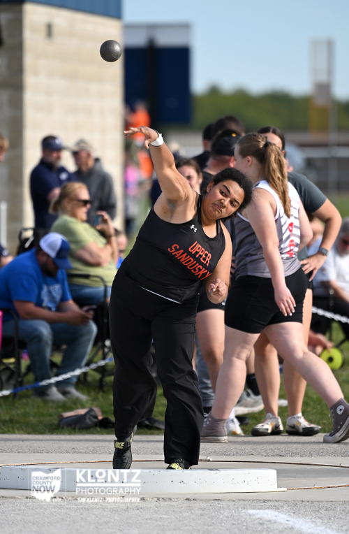 Female hammer thrower from Upper Sandusky releasing the hammer during an outdoor track meet, crowd watching in the background, action shot.